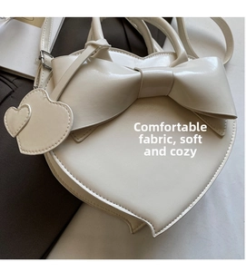 Détail d'un sac à main blanc en forme de cœur avec un grand nœud et cuir PU brillant