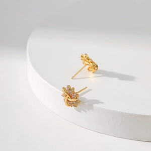 Detailed view of gold floral stud earrings with white zircons on a white pedestal