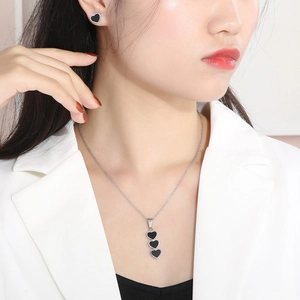 Close-up of a silver necklace and stud earrings set with black heart-shaped shell elements