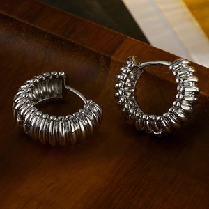 Pair of silver textured hoop earrings with unique ridge design on dark wood background