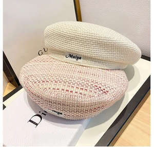 Detail of tweed beret hats in beige and pink weave featuring a stitched fabric label