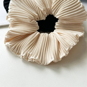 Macro shot of pleated satin hair scrunchies in beige and black with fine silk textures