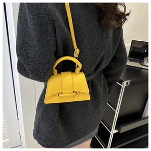 Detailed shot of yellow pebbled leather crossbody bag shown on a grey blazer outfit