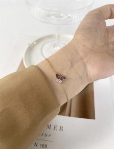 Detail shot of gold butterfly bracelet with purple and pink gemstones on a wrist