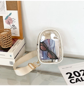 Transparent candy-colored PVC crossbody bag with white trim and beige strap on a glass table