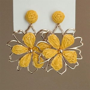 Detailed view of yellow woven flower earrings with gold metallic frames and textures
