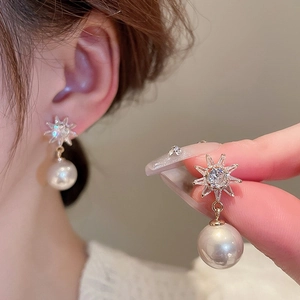 Detail of gold-plated starburst earrings with sparkling crystals and a white pearl drop