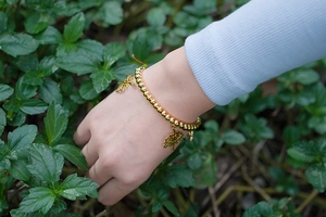 Bracelet à perles dorées avec breloques Arbre de Vie porté au poignet dans la nature