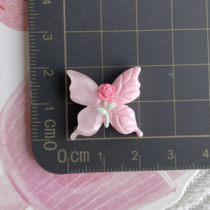 Macro view of a pink resin butterfly charm with a small rose and ruler for scale