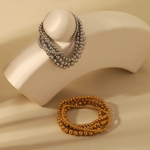 Detail of layered 18K gold and silver beaded elastic bracelets on a minimalist display