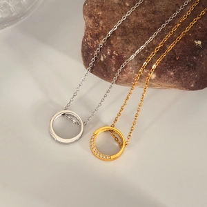 Close-up of gold and silver circle necklaces with pavé zircon detail on a stone surface