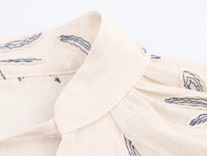 Detailed close-up of blue embroidery on a linen V-neck blouse with lantern sleeves