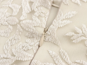 Dettaglio del ricamo in pizzo beige e cerniera invisibile su abito lungo elegante