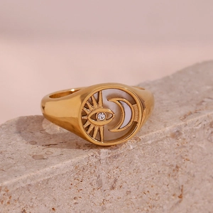 Detail of 18K gold-plated signet ring featuring sun, eye, and moon motifs on white shell