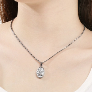 Macro shot of a silver miraculous medal pendant on a box chain worn by a model
