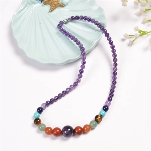 Detail of bohemian chakra necklace with purple beads and shell tray on white background