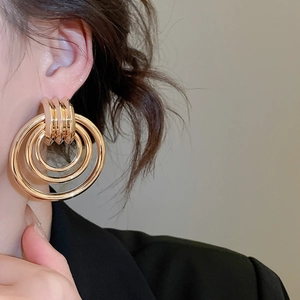 Nahaufnahme eleganter, dreilagiger goldener konzentrischer Creolen an einem Frauenmodell