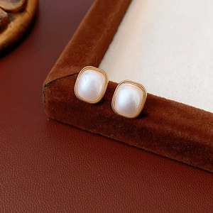 Macro view of square pearl earrings with gold metal frame on a brown leather background