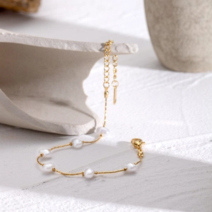 Elegant gold stainless steel bracelet featuring irregular white pearls on a stone surface