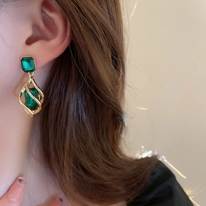 Close-up of vintage gold teardrop earrings with emerald green gemstones on model