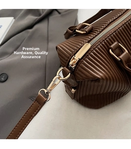 Close-up of light gold metal hardware and brown pleated leather texture on handbag