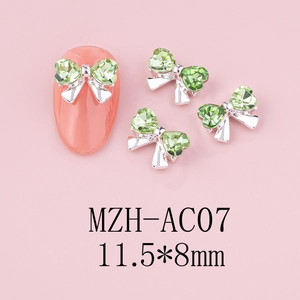 Macro detail of bow-shaped nail charms with light green rhinestones and silver base