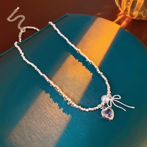 Detail of silver beaded necklace with pearl, bow, and pink heart gemstone pendant