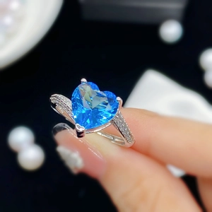 Primer plano de anillo plateado con gema azul de corazón y pavé de diamantes