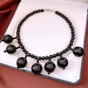 Detail of a black beaded necklace with round acrylic pendants in a white gift box