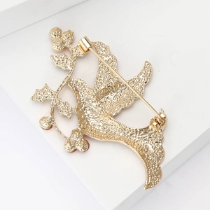 Macro view of golden bird brooch showing the textured metal back and pin clasp mechanism