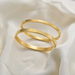Primer plano de brazaletes de acero inoxidable dorado sobre fondo de seda blanca