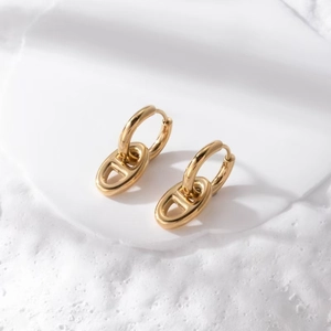 Detail of 18K gold polished stainless steel earrings with geometric links on marble