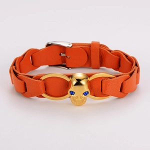 Detail of orange braided leather bracelet with golden skull and blue gemstone eyes