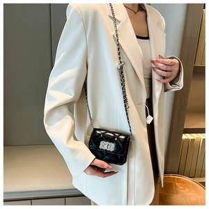 Close-up of black quilted chain bag with metal clasp worn by a woman in a white blazer