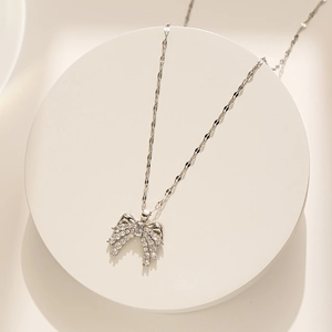 Elegant silver bow pendant necklace with sparkling zircon on a white display stand