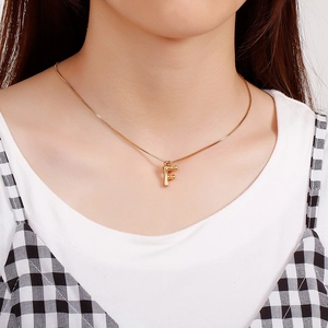 Golden necklace with bamboo texture letter F pendant on model in natural indoor light