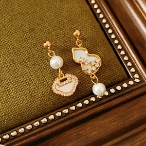 Detail of gold asymmetrical gourd earrings with zircon and mother of pearl on fabric