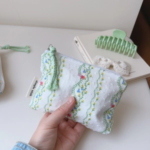 Détail d'une pochette en coton fleurie avec un gland et une étiquette simple wish