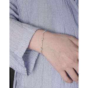 Minimalist S925 sterling silver bar and bead bracelet worn on wrist over purple fabric