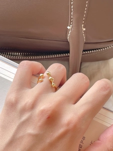 Close-up of golden irregular wavy minimalist ring worn by model on a warm aesthetic backdrop