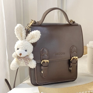 Brown vintage messenger bag with white plush bunny keychain accessory on wooden table
