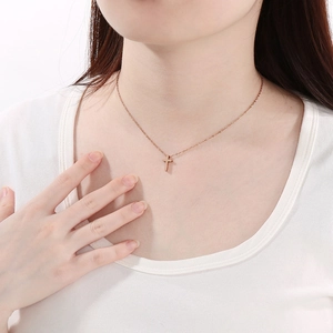 Close-up of a elegant rose gold cross pendant necklace worn by a female model on a white shirt