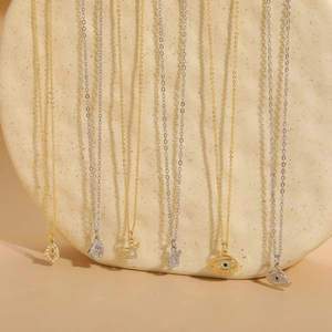 Evil eye and angel pendants on gold and silver plated chains over natural stone backdrops
