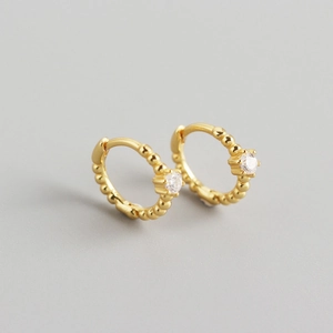 Detail of golden textured beaded hoop earrings with inlaid clear round gemstones