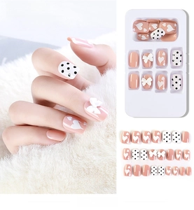 Macro shot of nude pink press-on nails with 3D bows and black polka dot designs