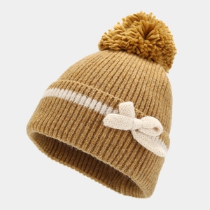 Close-up of ginger yellow ribbed knit hat with a soft pompom and cream bow detail