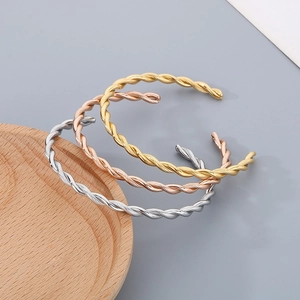 Macro shot of twisted metal texture on C-shaped open bangles in gold, silver, and rose gold