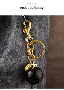 Detailed view of a golden metal keychain with a sleek black apple charm on a grey bag