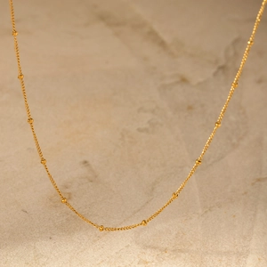 Détail macro d'un collier à billes doré minimaliste sur une pierre texturée claire