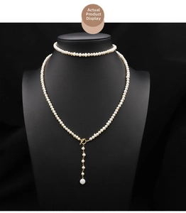 Detail of long natural pearl sweater necklace with golden T-bar clasp on black mannequin
